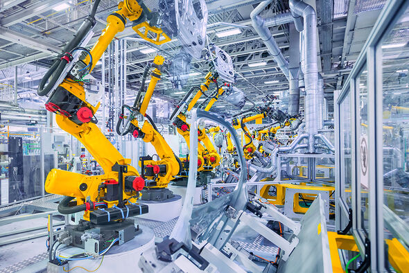In einer Produktionshalle stehen Robotermaschinen in einer Reihe.