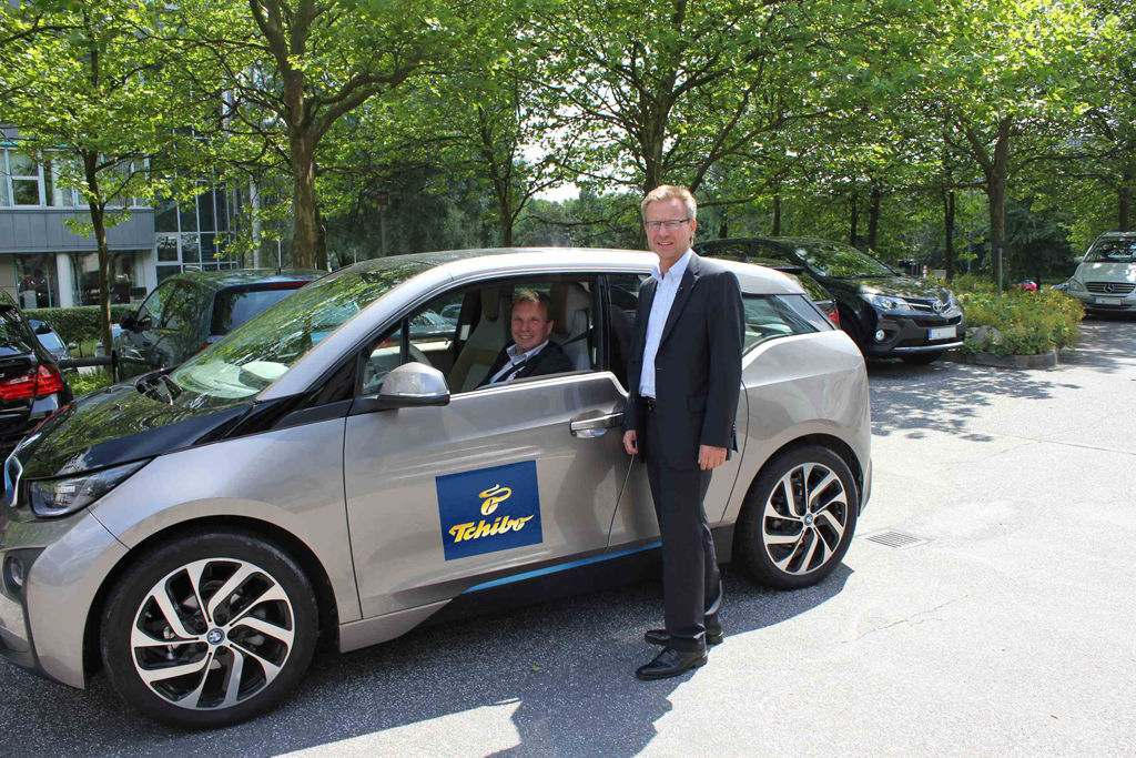 Freuen sich über die dritte „Grüne Karte“ der DUH für Tchibo in Folge: Fuhrparkmanager Oliver Komm (stehend) und Nachhaltigkeitsmanager Stefan Dierks im BMW i3 des Geschäftsführers Dr. Markus Conrad.