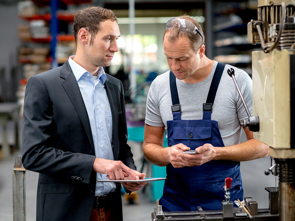 Ein Manager und ein Arbeiter sprechen in der Produktionshalle.