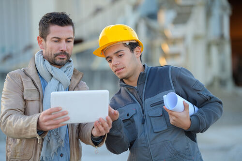 Ein Architekt und ein Bauarbeiter schauen sich digitale Baupläne auf dem Tablet an.