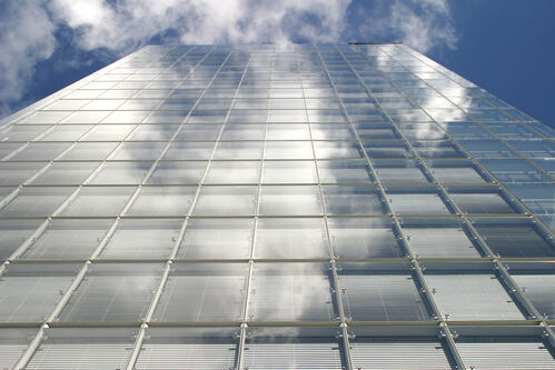 Eine Glasfassade spiegelt sich im Himmel mit Wolken.