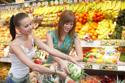 Zwei Frauen legen Gemüse in Ihren Einkaufswagen.