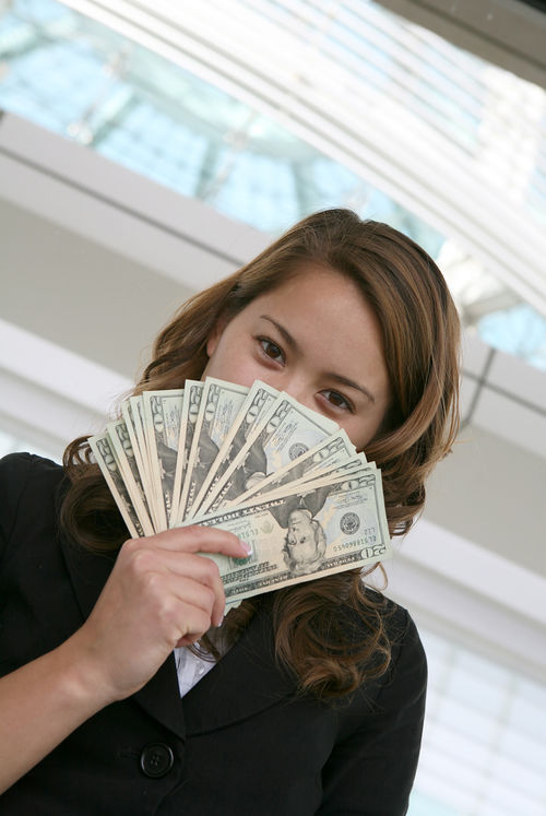 Eine Frau hält Geldscheine vor ihr Gesicht.