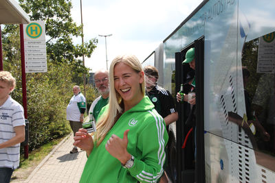 Ein Fan des Vfl Wolfsburg steht lächelnd vor dem Bus zum Spiel.