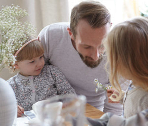 Ein Vater sitzt mit seinen zwei Kindern am Tisch und isst.