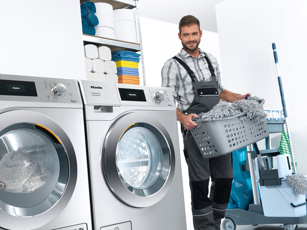 Ein Mann trägt Wäsche zu einer Waschmaschine